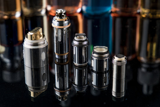 Electronic cigarette steel coils in a row with e-juice bottles in the background