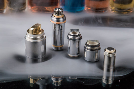 Electronic cigarette steel coils in a row with e-juice bottles in the background with misty smoke