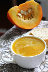 Pumpkin soup in white mug on table.