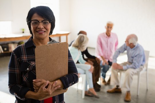 Portrait of senior female holding clipboard with friends sitting