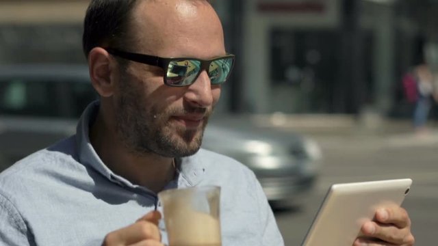 Young man using tablet computer and drinking coffee in cafe in city
