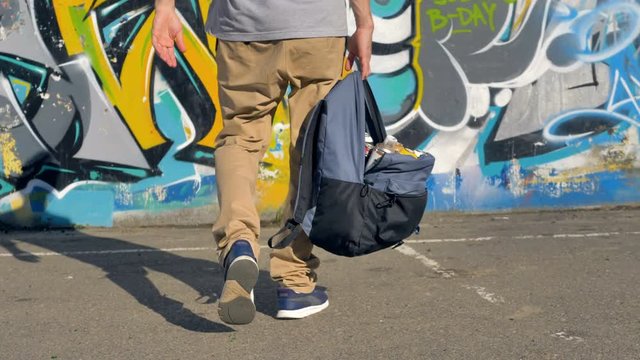 An open backpack with paint cans hangs from a male hand. 