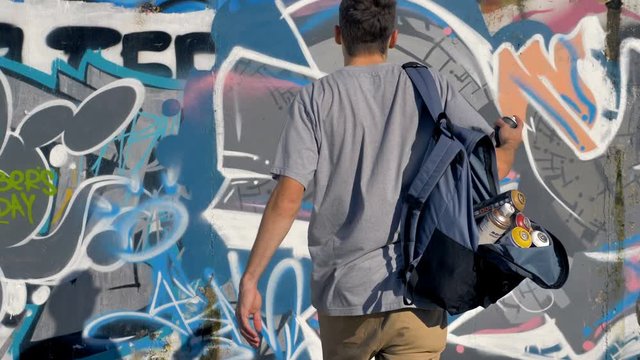A male graffiti artist adds another spray paint to a graffiti wall.
