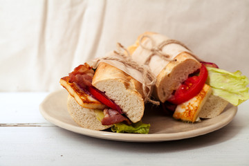 Fresh baguette sandwiches bahn-mi styled with bacon, roasted cheese, tomatoes and lettuce on white wooden background
