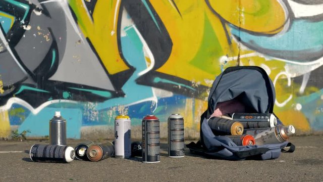Used spray paint cans in a backpack near a graffiti wall. 