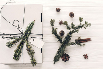 christmas present flat lay. stylish white christmas gift with empty tag and anise tree branches pine cones on rustic background top view, space for text. xmas seasonal greetings. winter holidays