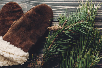 warm cozy gloves on rustic background with fir green branches top view, space for text. hipster stylish simple gloves and christmas tree. seasonal greetings. holiday mood