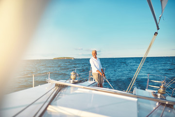 Fototapeta premium Mature man steering his sailboat on the open ocean