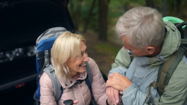 Joyful couple of elderly tourists staning near their car in the forest