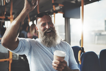 Bearded man standing on a bus drinking coffee and laughing