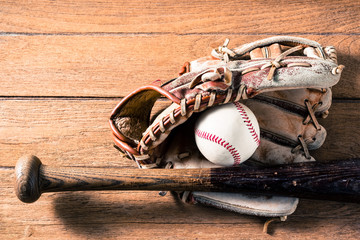 worn out baseball equipment on space of old wood, ( ball, baseball bat and leather glove )