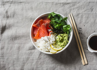 Smoked salmon sushi bowl on grey background, top view. Rice, avocado puree, salmon - healthy food concept. Asian style food