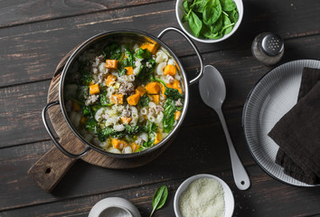 Sweet potato and pork sausage soup with spinach and pasta in a pot on dark background, top view. Delicious autumn, winter comfort food concept