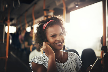 Smiling African woman standing on a bus listening to music