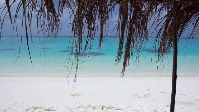 Perfect wild sandy Maldives beach with turquoise sea water and white sand. View through grass palm leaf sun umbrella, nobody, travel destinations 