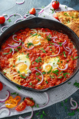 Tasty Breakfast Shakshuka in a Iron Pan. Fried eggs with tomatoes, red, yellow peppers, onion, parsley, Pita bread and herbs. Healthy Food