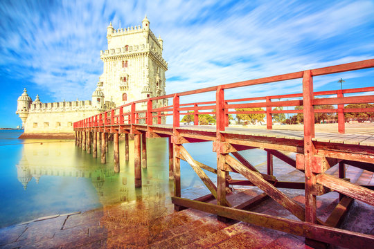 The iconic and spectacular Belem Tower and wooden jetty reflecting on Tagus River with low tides. Torre de Belem is Unesco Heritage and famous city landmark in Lisbon, Belem District, Portugal.