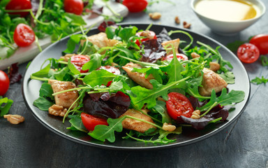 Fresh salad with chicken breast, arugula, nuts and tomatoes on black plate in a wooden table.