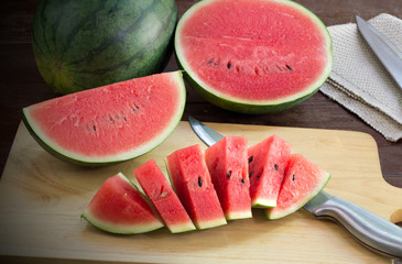 Watermelon slices on chopping board and knife all on wooden table