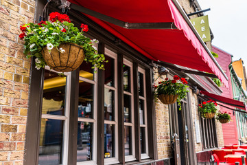 Red geranium flowers hanging in flower baskets by windows outside restaurant tables