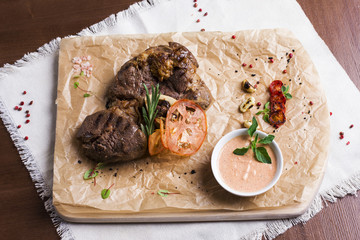 The large roasted piece of meat on the bone with sauce and spices on wooden board. View from top