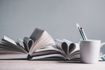 Books open in heart shape, a cup  and pens