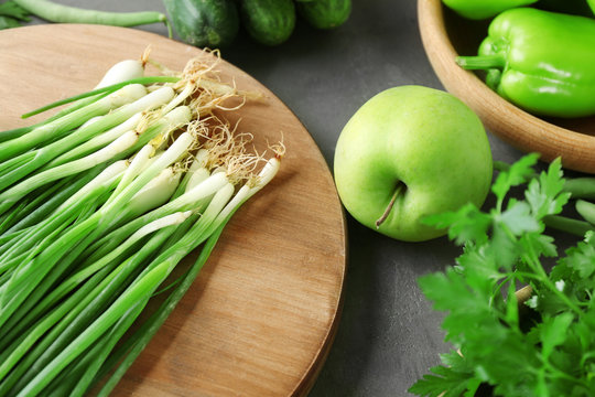 Wooden board with green onion and apple on table