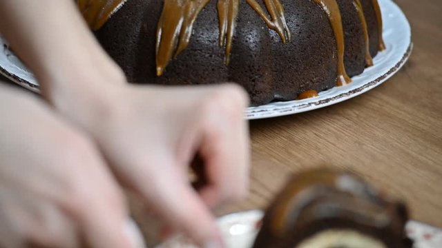 Girl cuts a piece of chocolate cake with cream cheese and puts it on a plate close-up shot