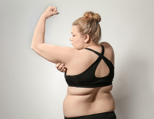 Woman touching fat on her arm against light background. Weight loss concept