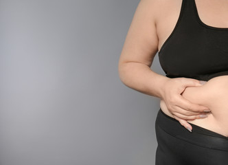 Woman touching fat on her belly against grey background. Weight loss concept