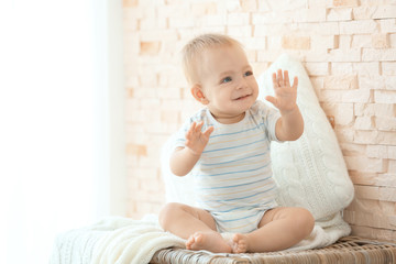 Fototapeta premium Cute little baby sitting on wicker box near brick wall