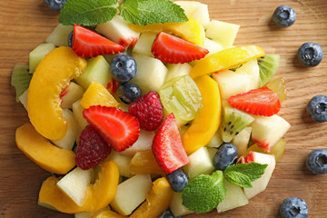Delicious fruit salad on wooden plate, closeup