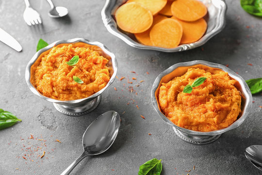 Metal bowls with mashed sweet potato on grey background