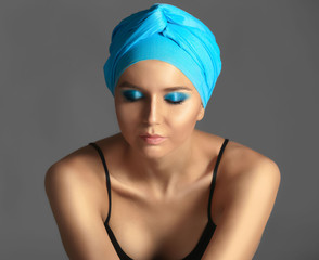 Beautiful young woman in blue kerchief against grey background