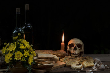 Skull and bread spoiled with wine bottle by candle light on wooden table with dim light in halloween night on dark background.Still life style and selective focus.