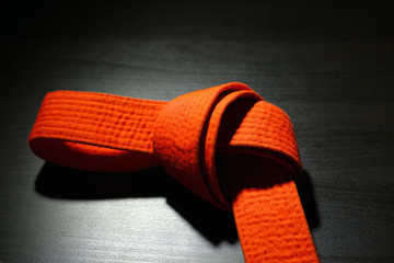 Orange karate belt on dark background © Africa Studio