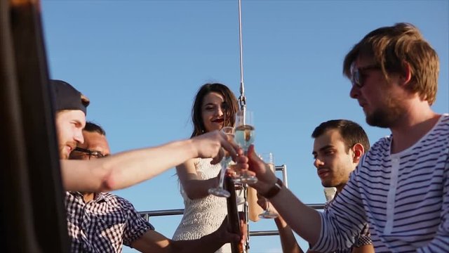 Young friends spend summer vacations on a yacht, friends drink alcoholic drinks from glass glasses, men and women who have fun time, clink glasses