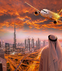 Obraz premium Arabski mężczyzna z samolotem lecącym nad Dubajem przed kolorowy zachód słońca w Zjednoczonych Emiratach Arabskich