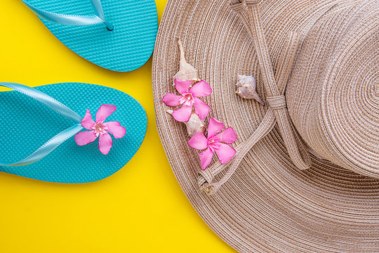 Women Straw Hat with Bow Pink Tropical Flowers Blue Slippers Sea Shells on Yellow Background Beach Vacation Seaside Traveling Fashion Flat Lay Copyspace