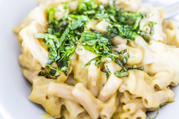 Macro closeup of homemade penne pasta with creamy sauce and fresh cut chopped basil leaves