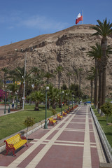 Morro de Arica towering over colourful benches and gardens of Plaza Vicuna McKenna in the coastal city of Arica in northern Chile.