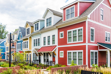 Fototapeta na wymiar Row of colorful, red, yellow, blue, white, green painted residential townhouses, homes, houses with brick patio gardens in summer