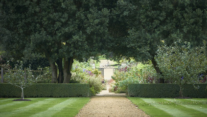 Pathway to an ornate wrought iron gate through landscaped gardens