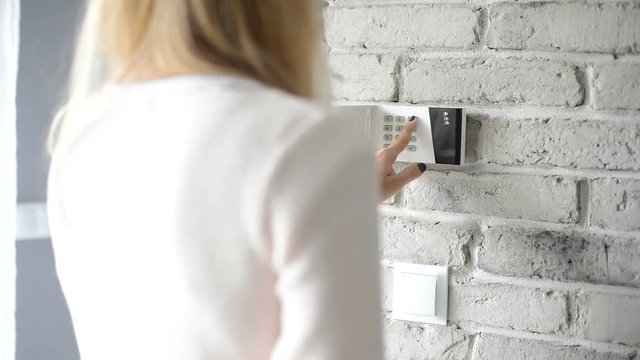 Woman entering pin on home security alarm keypad on the wall