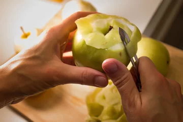 Fotobehang Female hands peeling skin off of green apple using a paring knife. Peel the Skin Off Apples. Woman cuts off the peel of an apple. Garden apples. Golden apples. Farm products. Juicy fruit. © colorshadow