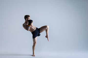 Fototapeta na wymiar Horizontal picture of mixed fight man in trunks and gloves practising kicks in spacious studio. Attractive professional male kickboxer training in gym. Sports, endurance, determination and activity