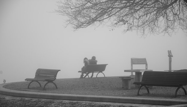 Lonely couple on the bench, besides lake on foggy morning
