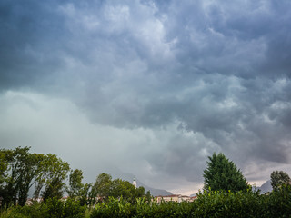 Obraz premium Thunderstorm clouds over trees and bell tower, Belluno, Veneto, Italy
