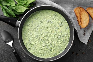 Frying pan with tasty spinach sauce on table