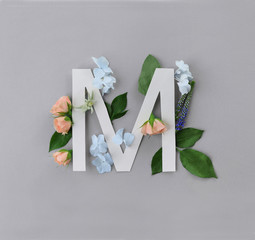 Composition with letter M and beautiful flowers on color background